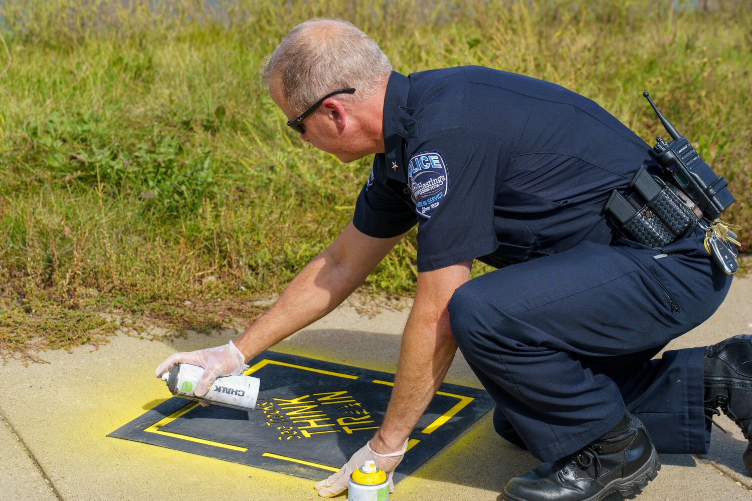 Police Chief David Wilske took his turn chalking the “See Tracks, Think Trains” logo on a sidewalk at the 2nd Street East railroad crossing. The paint is actually a non-permanent spray chalk that should last a week or two depending on the weather.