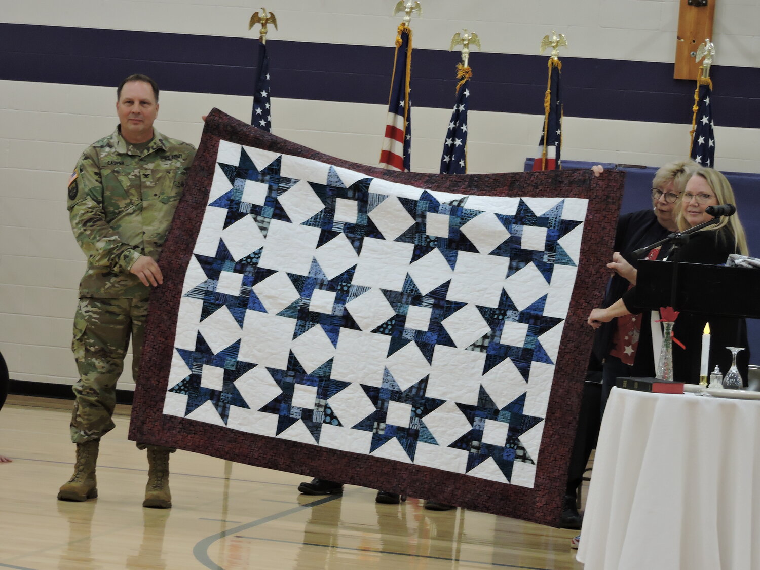 Lt. Col. Ryan Casper, a retired Ellsworth High School social studies teacher with 40 years of military service, receives the Quilt of Valor from Kathy Krug and Laura Cutsforth.