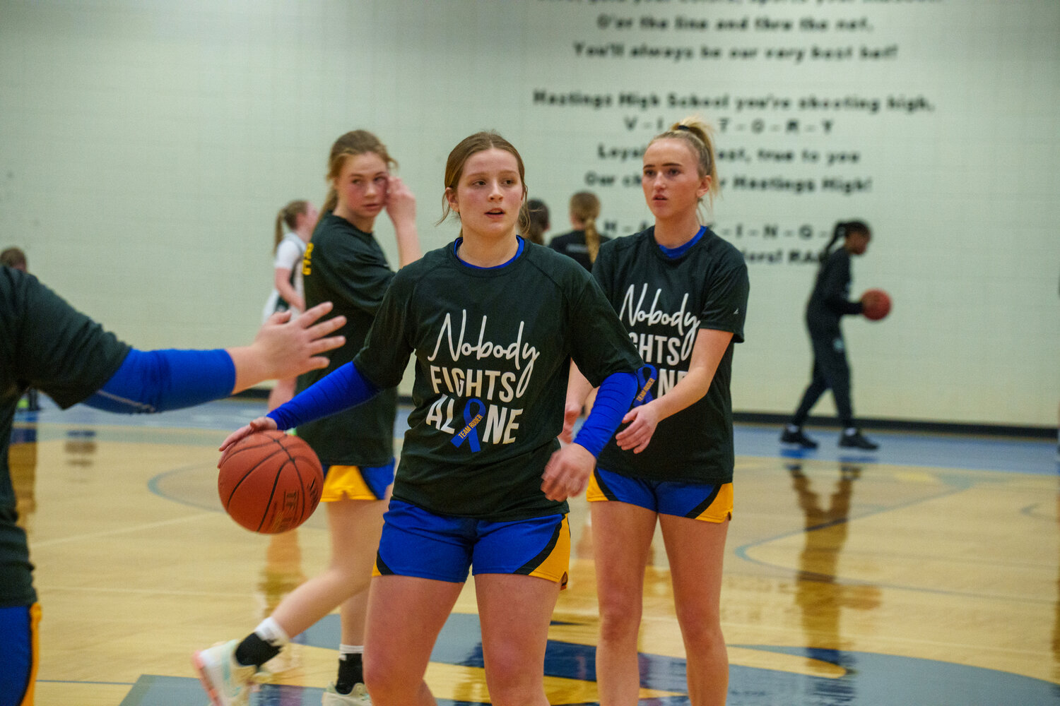 The season opener for Hastings included a special moment for the Ruder Family. Junior Kate Ruder and many of the girls on the varsity roster have been coached by Kate’s father, Bill. Bill was diagnosed with cancer back in October. The team decided to wear special warm-up shirts for the season that says ‘Nobody Fights Alone’.