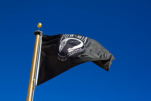 Sunlit black POW-MIA flag flying in a brilliant blue sky. Copy space available.