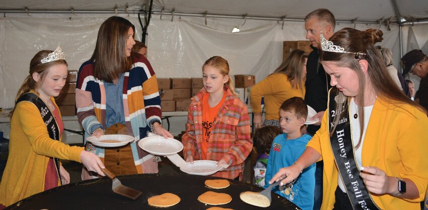 Honeybee Festival royalty lends a hand Friday morning in the Kiwanis Pancake Tent. Left Junior Miss Madi Grace Slaven serves hot pancakes from  the griddle, and Honeybee Queen Abigail Sanders, right, has cooking duty.