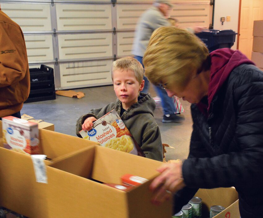 Abel Sullivan (left) is a third-generation helper for the Edgar County Community Nurse Association and its Christmas Basket program. Sullivan helped assemble food baskets with volunteer Lugene Joines (right). Sullivan&rsquo;s dad Matt Sullivan (not pictured) and grandpa Greg Sullivan (not pictured) are longtime volunteers.