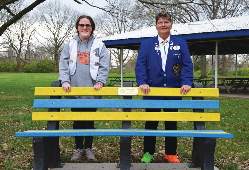 Gracie Wilson, left, and Amy Hill, right, show off one of several park benches made from recycled plastics donated by the Paris Lions Club. Local Lions and Leos (Junior Lions) have collected and cleaned caps, lids and pop tabs annually for several years.