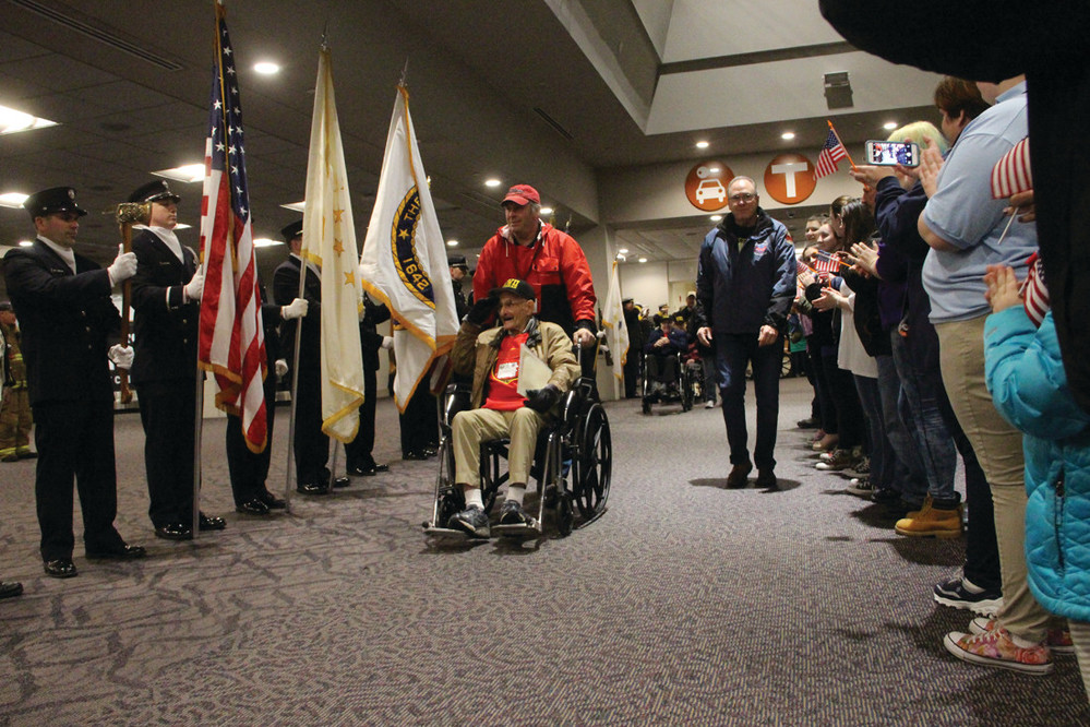 THEIR SERVICE RECOGNIZED: Accompanied by Russell DesGrange, who served as his guardian, WWII veteran Irwin Kaplin of Wakefield is saluted as he arrives at Green Airport for Saturday&rsquo;s honor flight to Washington, D.C.