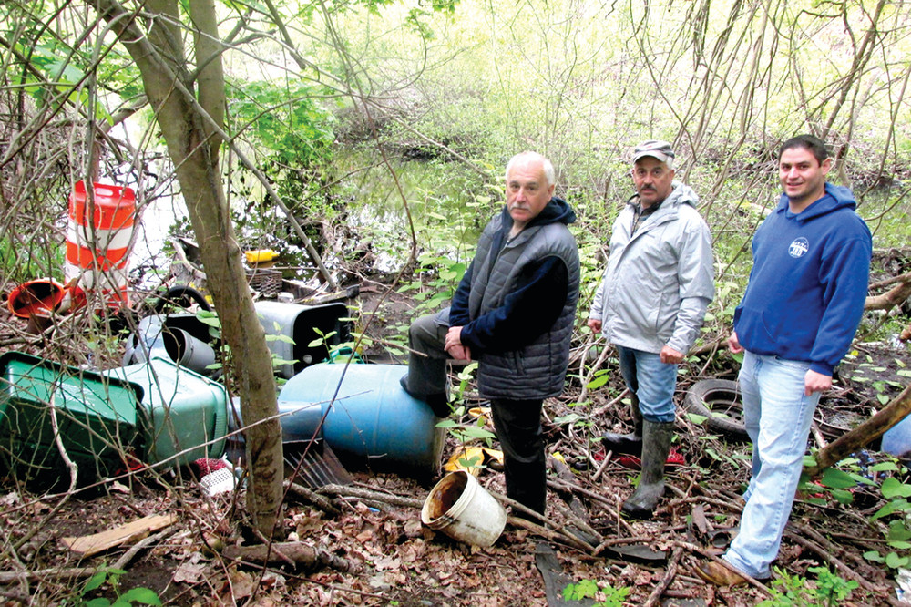 DAMAGING DEBRIS: Johnston Mayor Joseph Polisena, who is joined by Michael Maddalena of the Pawtuxet River Authority and District I Councilman Richard J. DelFino III, puts his foot on this large garbage container and looks around at other debris that people continue to dump alongside the once beautiful waterway.