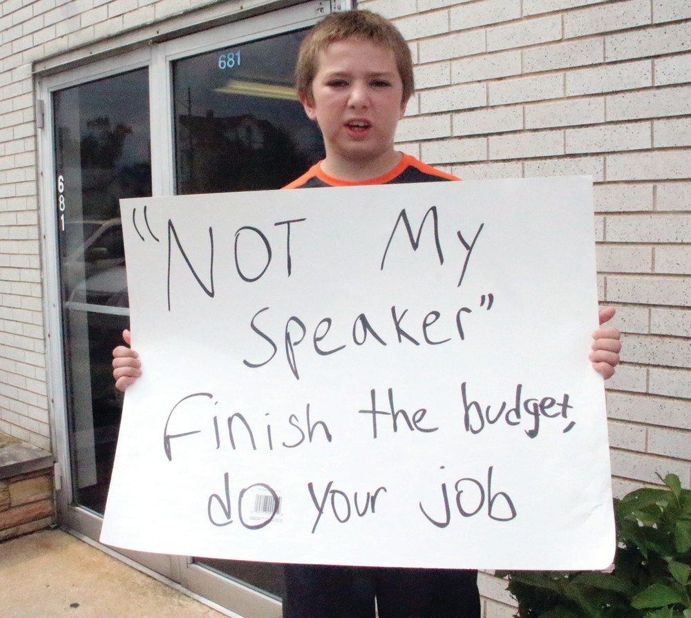 HOLDING FIRM: John Hanley, 10, remained outside the law offices of House Speaker Nicholas Mattiello as his father George and others protesting the lack of a state budget went inside to see Mattiello. &ldquo;I want him to get back to his job [at the State House],&rdquo; John said of Mattiello.