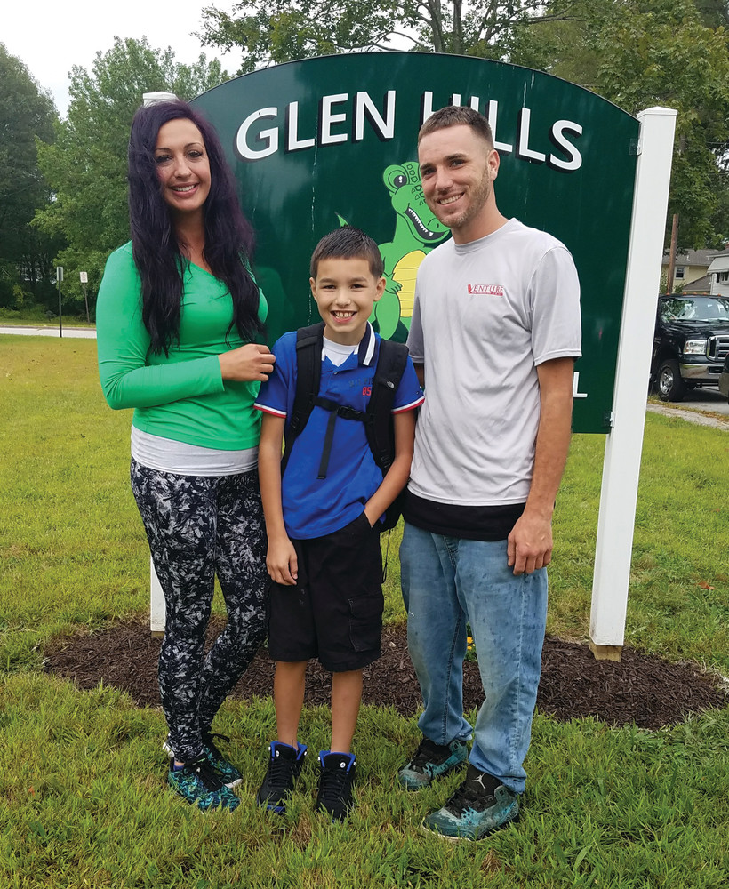 HEADING INTO THE FIFTH GRADE: Christopher Donnelly takes a moment to pose in front of the Glen Hills Gator sign at Glen Hills Elementary School during drop-off time on Tuesday morning. With him are James Donnelly and Heather Barber. (Herald photo by Jen Cowart)