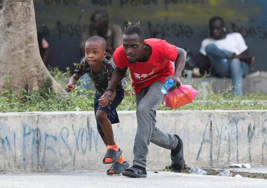 A man and child take cover from gunfire near the National Palace, in Port-au-Prince, Haiti, March 21, 2024.