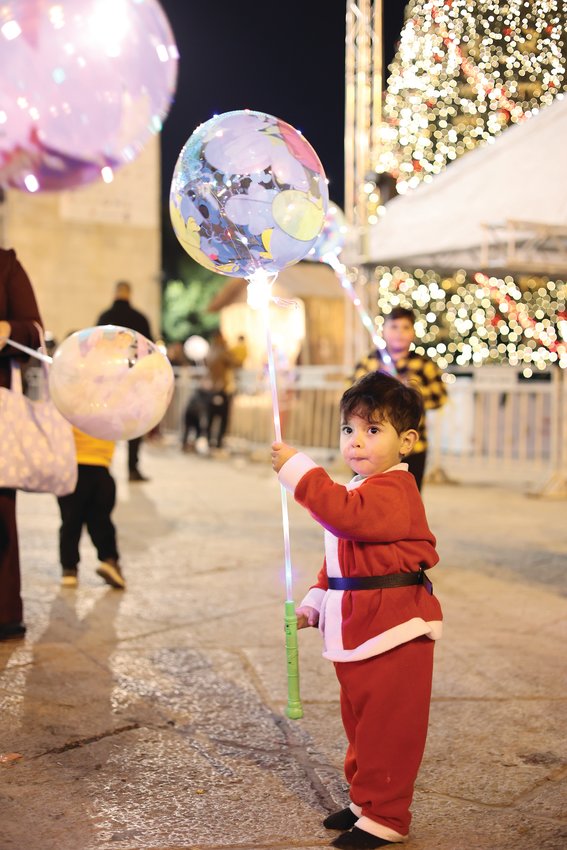 Dressed in Santa  suit, a young boy enjoys a  festive balloon, a popular  item for sale in  Manger Square. 
