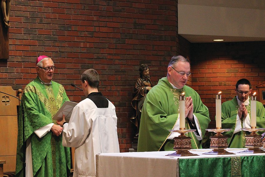 Father Michael McMahon professes his oath at the altar as Bishop Thomas J. Tobin installs him as the new pastor of St. Philip&rsquo;s Church, with Assistant Pastor  Father Phillip Dufour, at right.