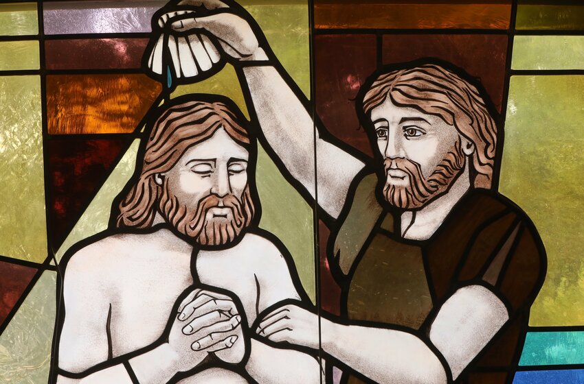 The baptism of Christ by John the Baptist is depicted in a stained glass window.