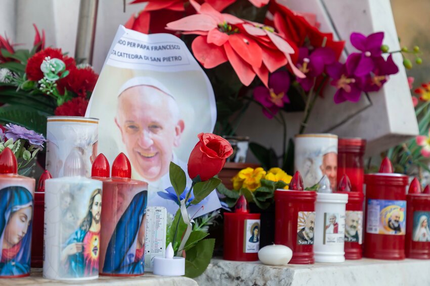 Votive candles and flowers are seen at the base of a statue of St. John Paul II outside Rome's Gemelli hospital Feb. 23, 2025, where Pope Francis is being treated for double pneumonia.