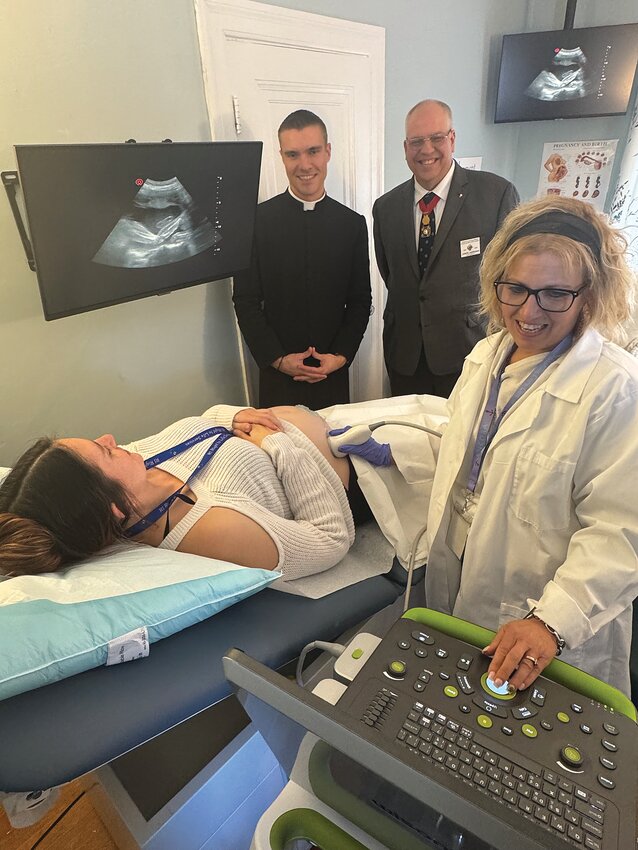 RI Right to Life sonographer Tracy Laberge tests the new machine by performing an ultrasound on fellow staff member Alex Bergeron, who is pregnant, as Father Mark Gadoury, Knights of Columbus state chaplain, and State Deputy Joseph Carrignan look on. The Knights of Columbus donated the $32,500 machine to RIRTL.