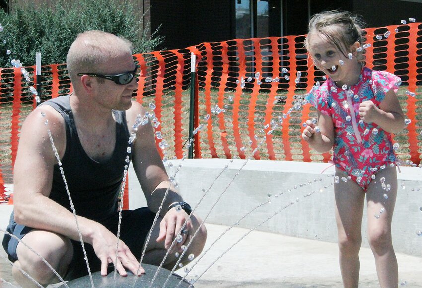 Travis Frederick, of Milford, has to coax his daughter, Jazlyn into the streams of water June 24 at the new spash pad in the uptown city park in Milford.