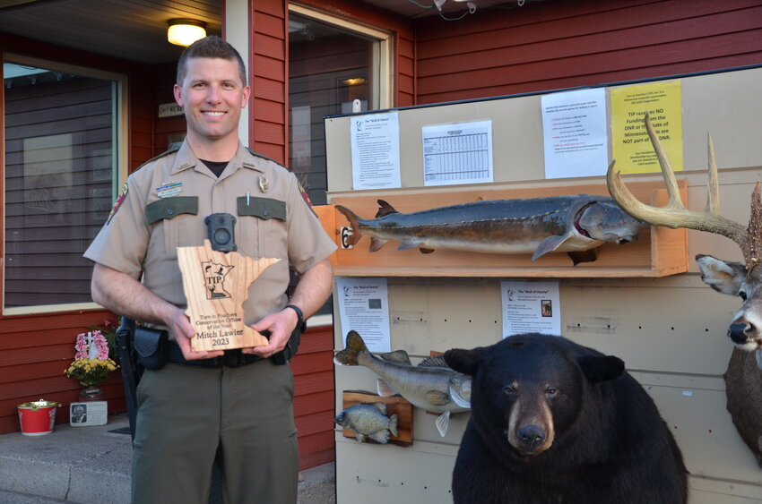 The Turn in Poachers 2023 Minnesota Conservation Officer of the Year Mitchell Lawler holds a plaque recognizing the distinction April 13 outside of Mr. Jim’s in Foley. Lawler stood in front of the TIP Wall of Shame, featuring animals confiscated from poachers.