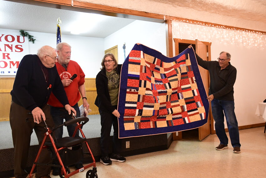 Mel Roehrl (from left) and Nick Johnston look at a Hugs of Gratitude quilt held by Roehrl’s daughter Deb Duclos and son Joe April 19 at the Melrose American Legion in Melrose. The quilt was presented to Roehrl by Johnston for Roehrl’s World War II service in the Navy.