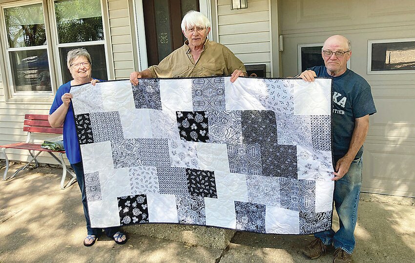 The quilt made by Chuck Wooley, center, with his wife Julie at left and friend Kenny Barrett at right. Kenny’s long arm was used to finish the quilt.