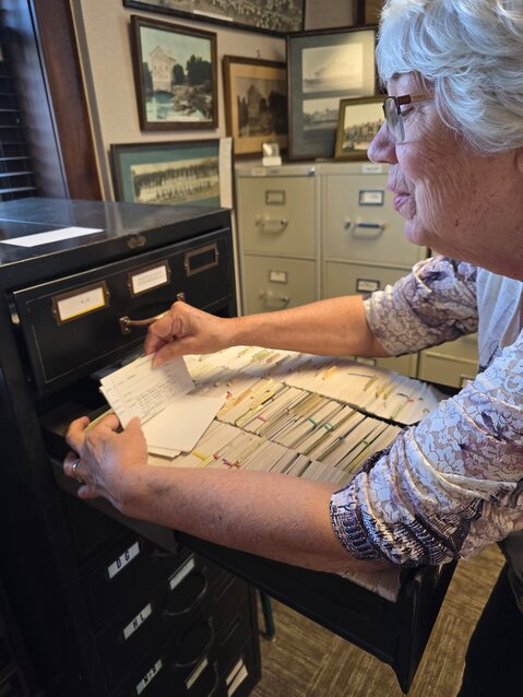 Margaret Woltman demonstrates the index card system. The cards are in alphabetical order by name, subject, place, or event and each card is marked with the corresponding location of the material.