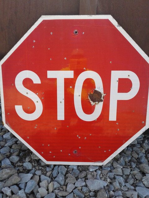 This stop sign has been targeted with a firearm, likely a shotgun blast. There are also signs of potshots with BB guns or buckshot.