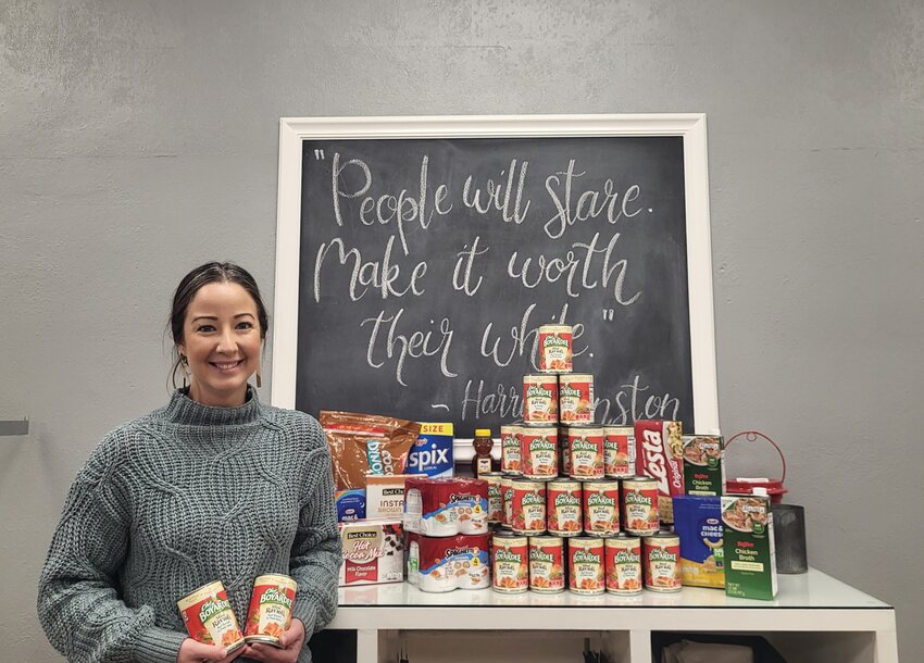 Jen Claussen, owner of Swans Apparel, poses with some of the canned goods that have been donated as part of the Hunger Games food drive.